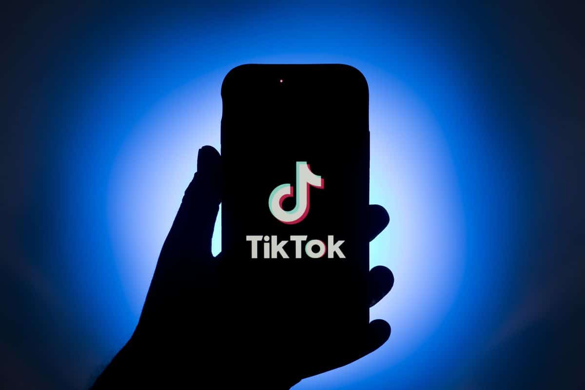 Image of the silhouette of a hand holding a mobile phone, with the logo and name 'TikTok' on the screen
